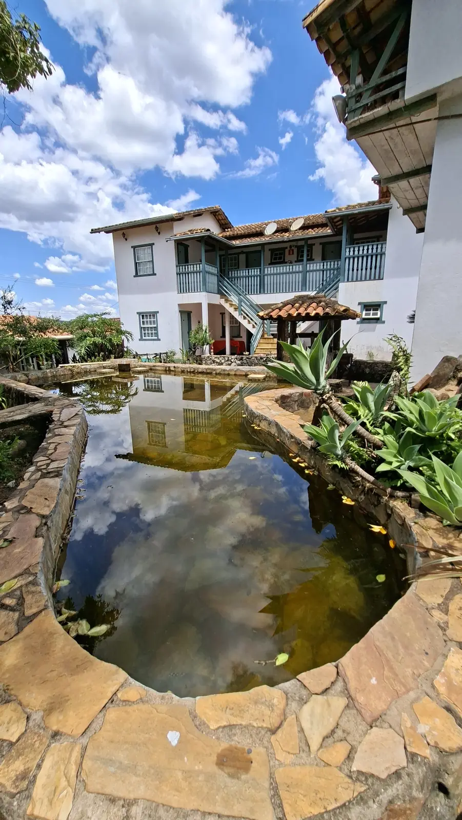 Piscina de água natural refletindo o céu, com a fachada da pousada ao fundo