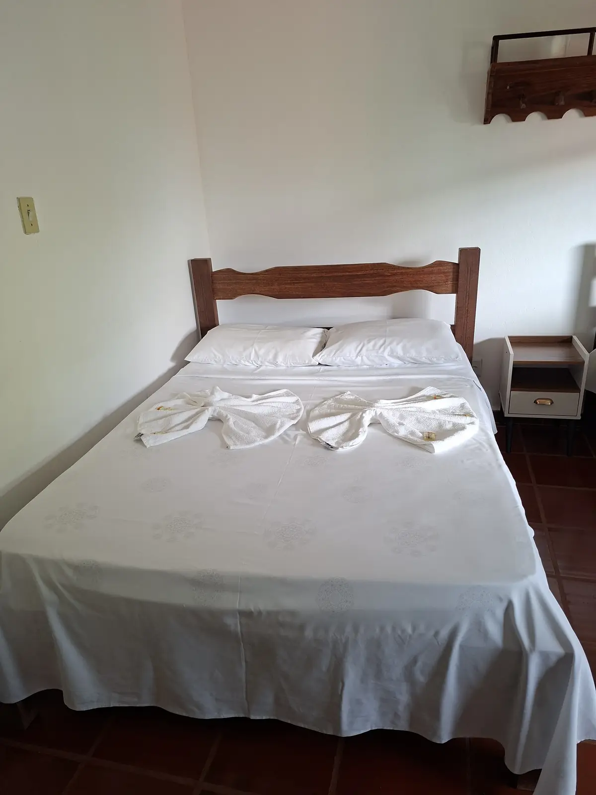 Cama de casal com enxoval branco e toalhas dobradas