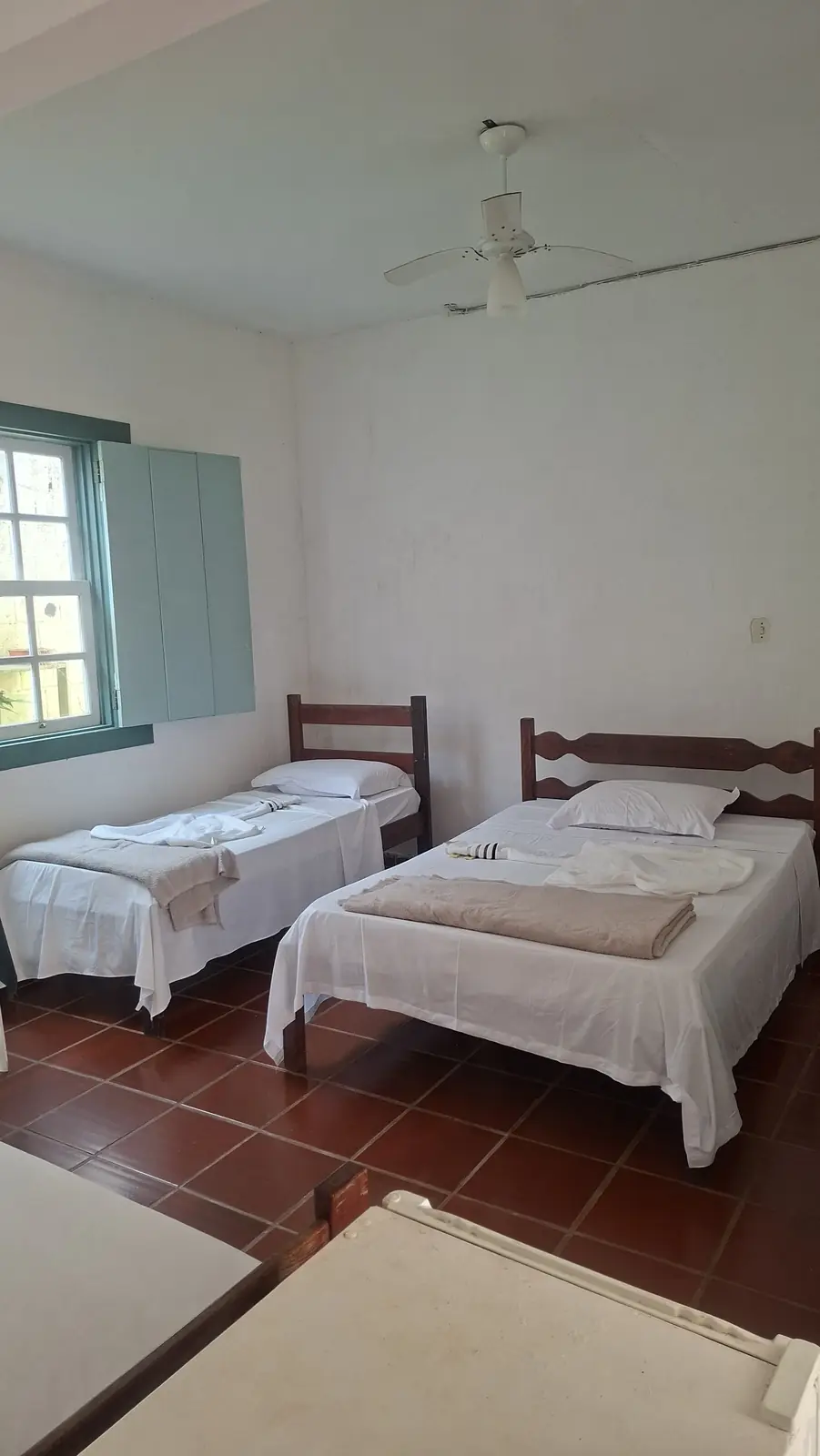 Acomodação com duas camas de solteiro, janela e ventilador de teto