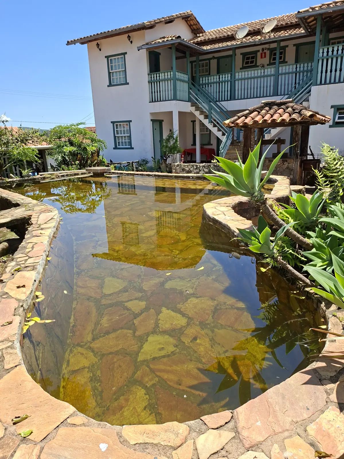 Piscina de pedra com água natural em frente à fachada da pousada